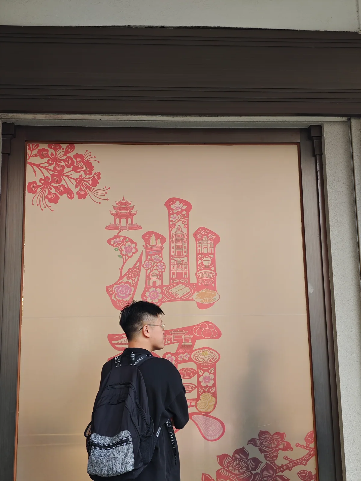 A traveller with a black backpack stands before a decorative Shantou panel / 背着黑色双肩包的旅人站在汕头主题装饰画前